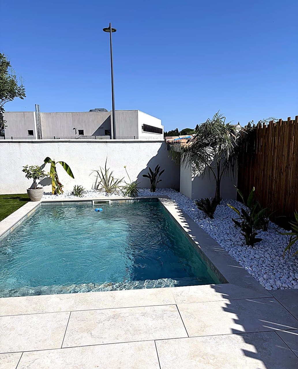 Piscine avec plage en pierre claire et massifs de galets blancs près de Nîmes